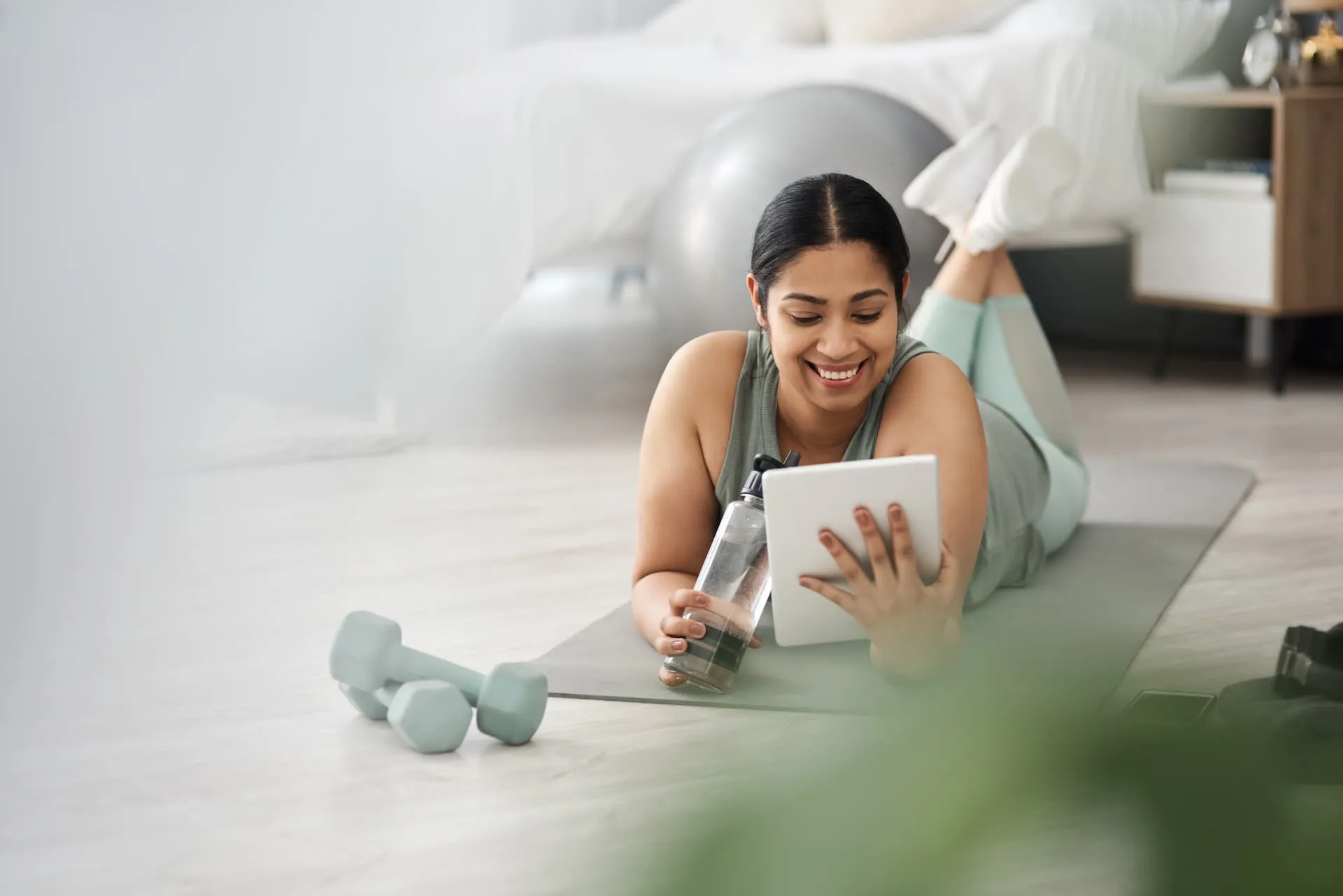 woman on her stomach smiling while looking at the tablet